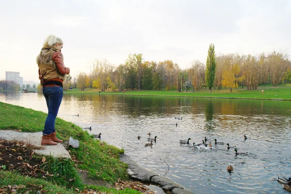 Dívka krmí kachny na rybníku v parku na podzim — Stock fotografie