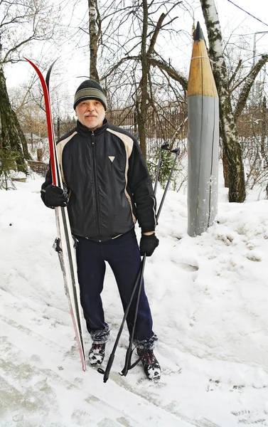 Un anciano de pie con un esquí de fondo en el parque en invierno — Foto de Stock