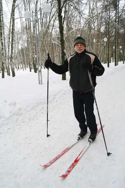 Un homme âgé se tient debout sur le ski de fond dans le parc en hiver — Photo