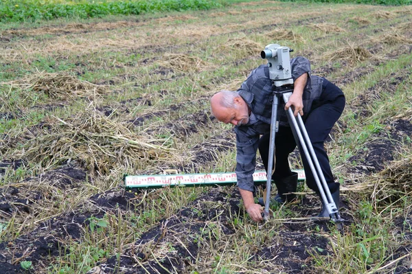 Een oudere man met een theodoliet voor het meten van de afstand veld — Stockfoto