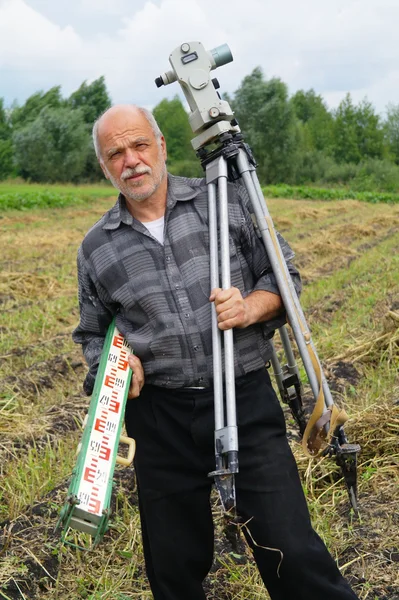 Un uomo anziano con un teodolite per misurare il campo di distanza — Foto Stock