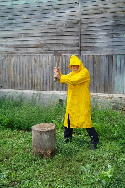 An elderly man in a yellow raincoat with an ax against the wall — Stock Photo, Image