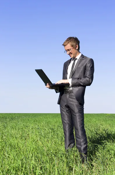 Framgångsrik, säker affärsman på gröna fält med en bärbar dator — Stockfoto