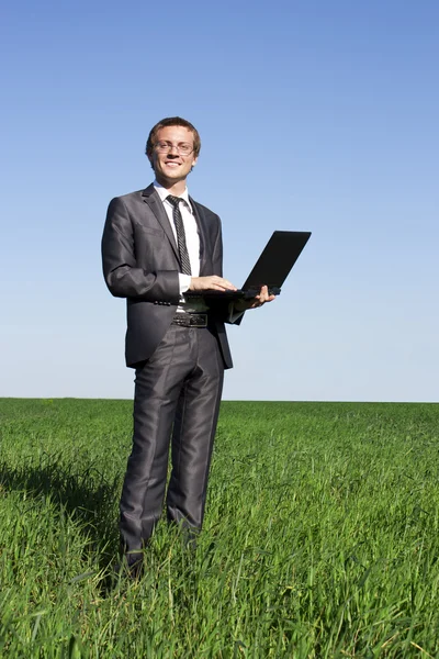Uomo d'affari di successo e fiducioso su un campo verde con un computer portatile — Foto Stock