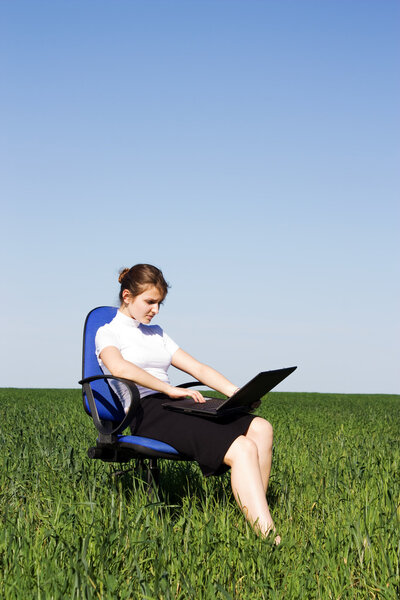 Serious businesswoman sitting on armchair outside and typing on