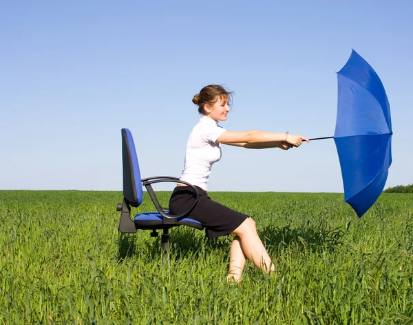 Businesswoman sitting on a field in a chair with umbrella — Stock Photo, Image