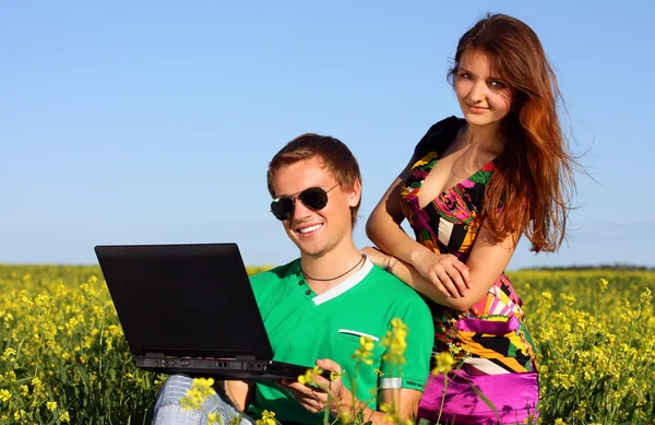 Bella giovane coppia in un campo con un computer — Foto Stock