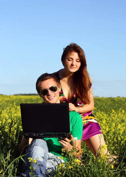 Όμορφο νεαρό ζευγάρι σε ένα πεδίο με έναν υπολογιστή — Φωτογραφία Αρχείου