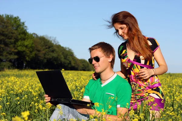 Belo jovem casal em um campo com um computador — Fotografia de Stock