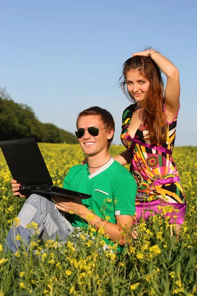 Krásný mladý pár v poli s počítačem — Stock fotografie