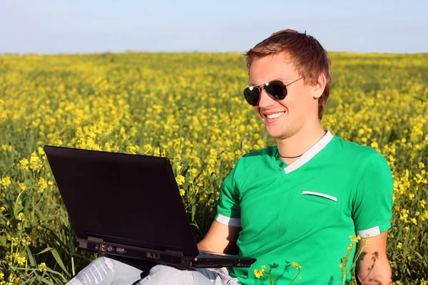 Ung kille med en bärbar dator som sitter i ett fält — Stockfoto