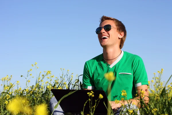 Laughing young man on a yellow field with a laptop — Stock Photo, Image
