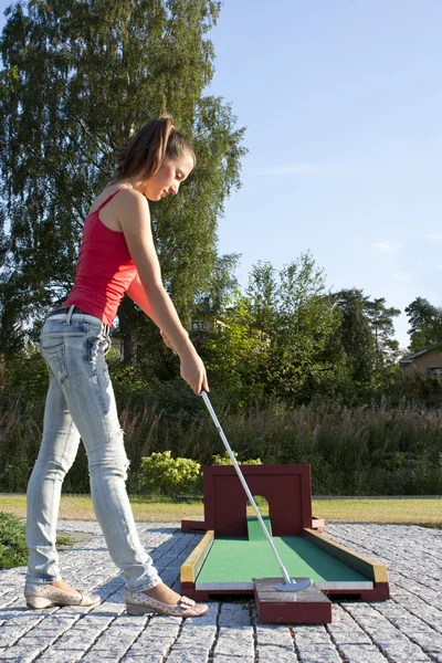 Atractiva joven mujer poniendo pelota de golf en verde con bosque en — Foto de Stock