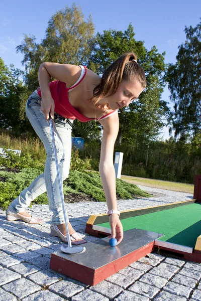 Attraktive junge Frau legt Golfball auf Grün mit Wald in — Stockfoto