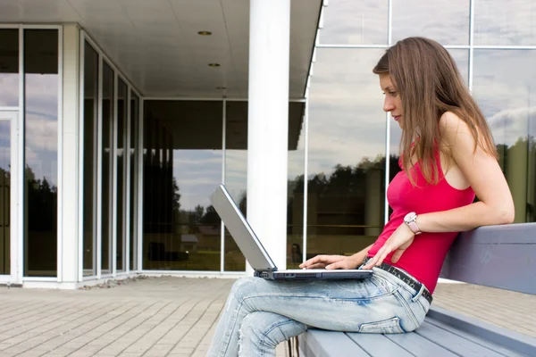 Jonge brunette op een bankje met laptop — Stockfoto