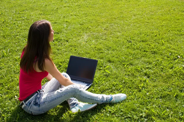 Linda chica adolescente sentada en la hierba estudiando con su lapto — Foto de Stock