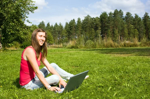 Молодая женщина печатает на ноутбуке снаружи на траве — стоковое фото