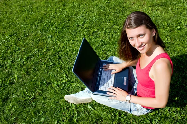 Morena bonita com um laptop em um gramado verde — Fotografia de Stock