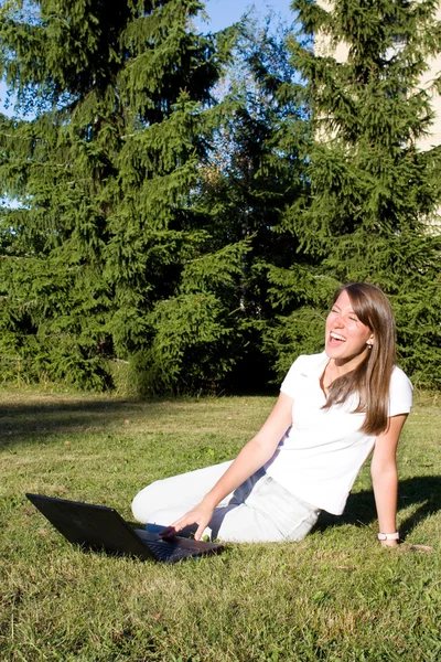 Счастливая девушка на траве с ноутбуком — стоковое фото