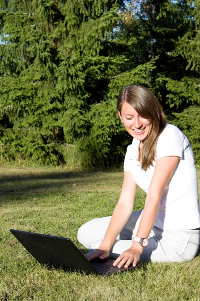 Menina sorridente com um laptop em um gramado — Fotografia de Stock