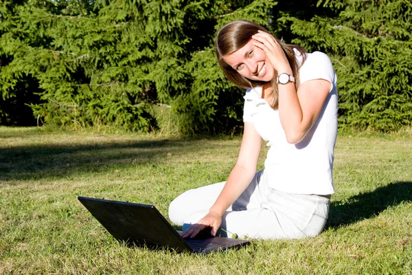 Χαμογελαστό κορίτσι με ένα φορητό υπολογιστή σε έναν χορτοτάπητα — Φωτογραφία Αρχείου