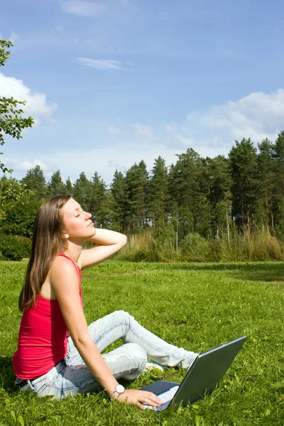 Young woman typing on a laptop outside on the grass Stock Photo