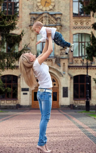 Щаслива молода жінка піднімає сина високо — стокове фото