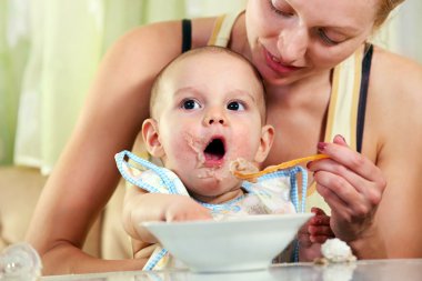 Mother feeding baby with spoon clipart