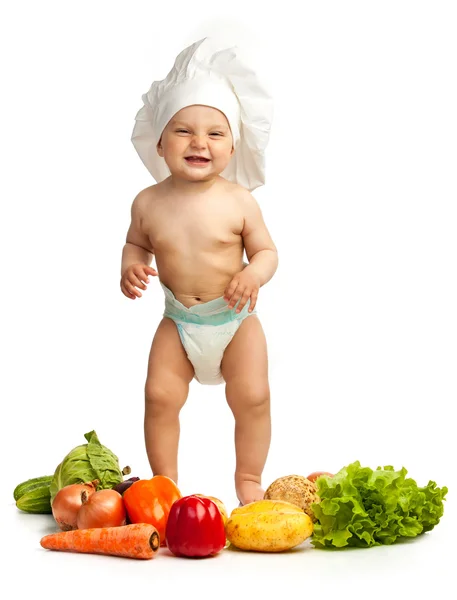 Μικρό αγόρι στο καπέλο του σεφ μεταξύ φρέσκα λαχανικά — Φωτογραφία Αρχείου