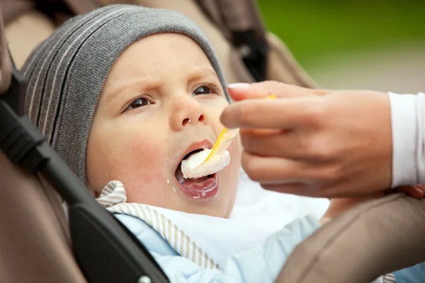 Mamma alimentazione di un anno vecchio ragazzo seduto nel passeggino — Foto Stock