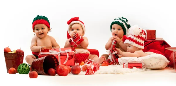 Cuatro bebés en trajes de Navidad jugando entre regalos — Foto de Stock