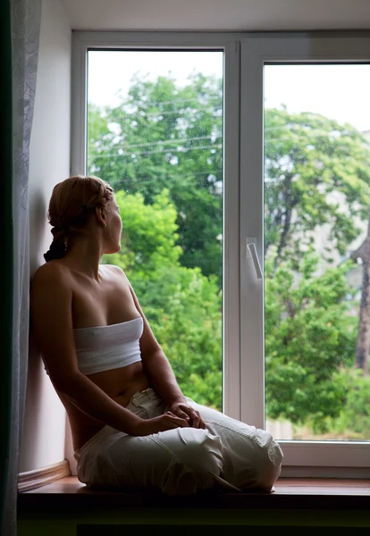 Młoda kobieta siedząca przez okno — Zdjęcie stockowe