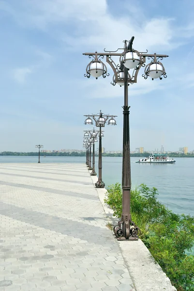 stock image The lamp poles at the bank against blue water and blue sky