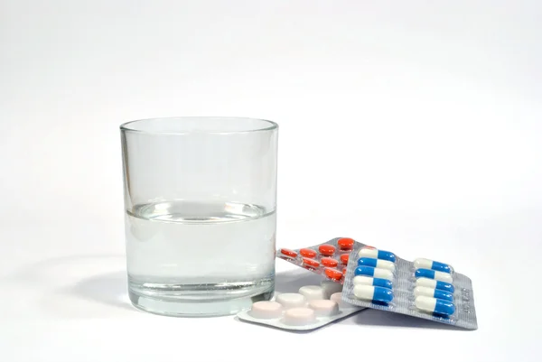 Het glas van water en containers met pillen — Stockfoto