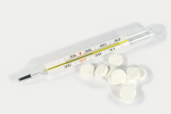 De clinical thermometer en witte pillen — Stockfoto