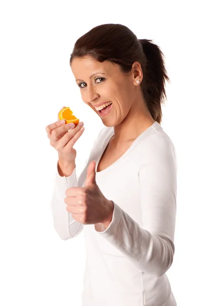 Carino giovane ragazza mangiare una fetta di frutta arancione mostrando pollice in su — Foto Stock