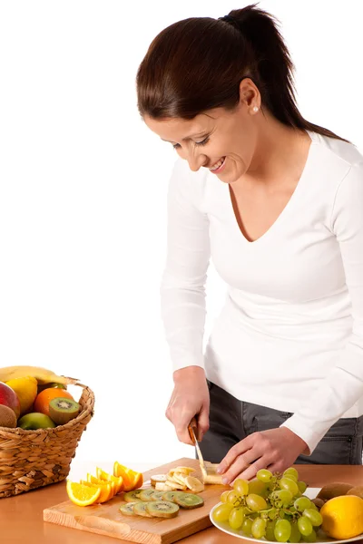 Attraktive junge Frau schneidet Früchte und bereitet Obstsalat zu — Stockfoto