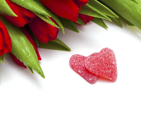 Red tulips and two heart-shaped candies — Stock Photo, Image