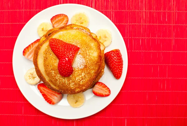 Golden buttermilk pancakes with strawberry and banana on red — Stock Photo, Image