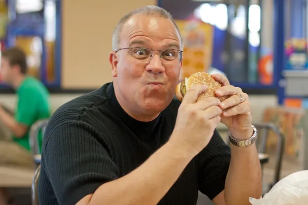 Mand spiser burger i fastfood restaurant - Stock-foto