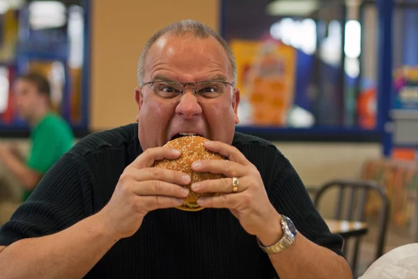 Un homme mange un hamburger dans un fast-food — Photo