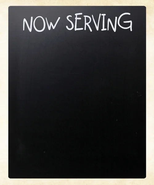 "Ahora servir "escrito a mano con tiza blanca en una pizarra — Foto de Stock