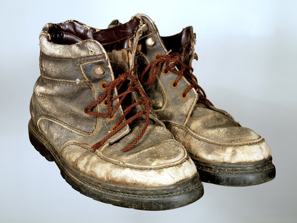 The old worn out boots with brown laces on a neutral background.