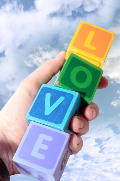 Liebe in hölzernen Spielblockbuchstaben in der Hand gegen Wolken — Stockfoto