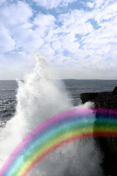 Giant wave crashing on coast cliffs with rainbow — Stock Photo, Image