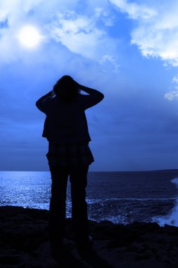 Silhouette of a sad lone woman on cliff edge clipart