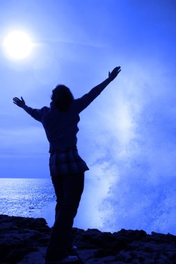 Silhouette of lone woman facing a wave on cliff edge clipart