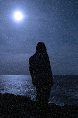 Silhouette of lone woman on cliff edge during rain shower clipart