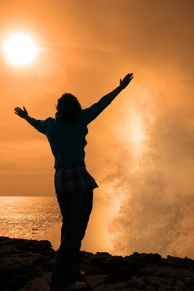 Silhouette einer einsamen Frau, die einer mächtigen Welle im Sonnenschein gegenübersteht — Stockfoto
