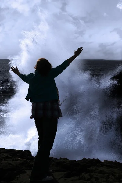 Silhouette of lone woman facing a powerful wave on cliff edge — Stock Photo, Image